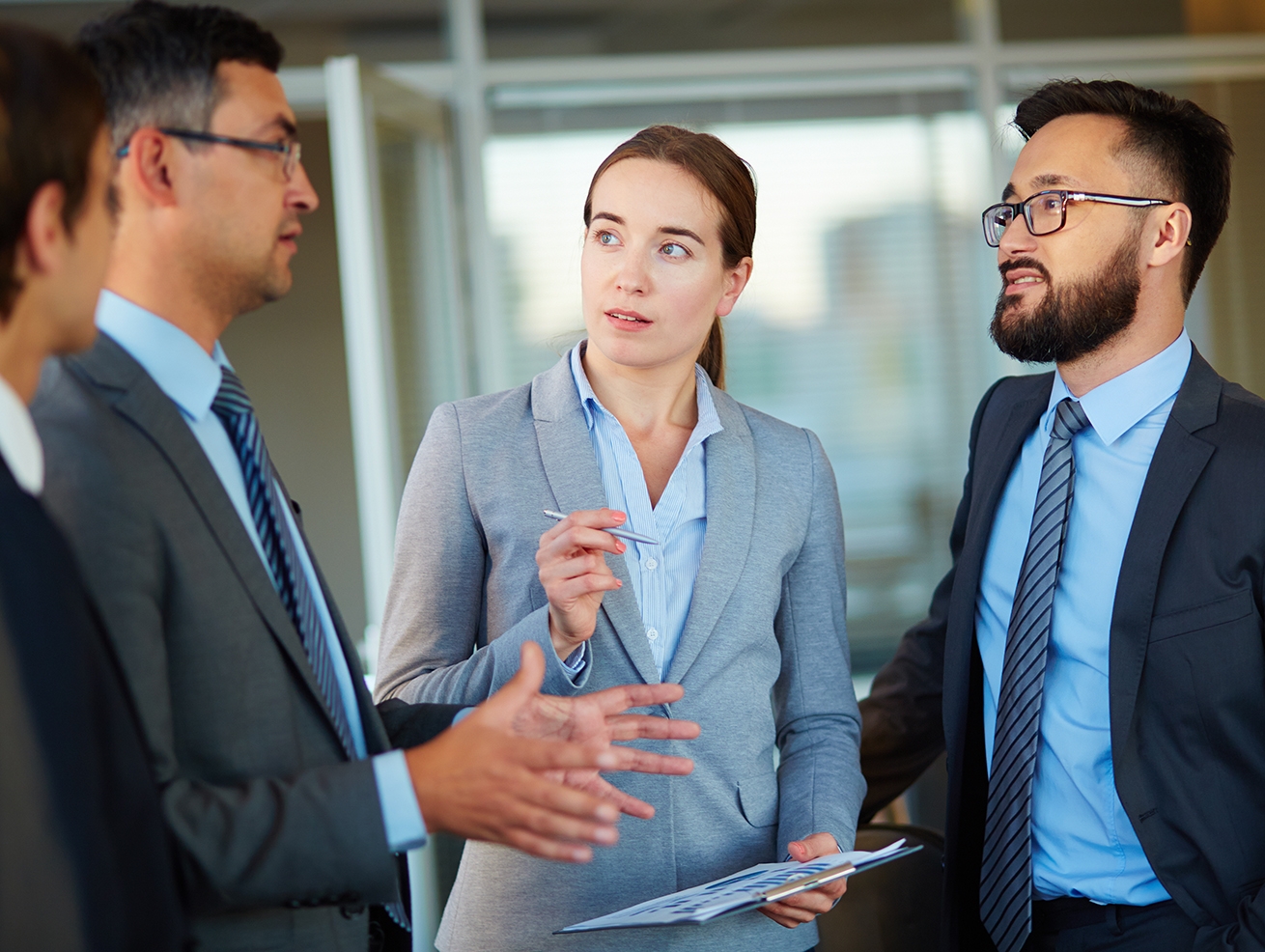 A female lawyer wearing a pale grey suit discussing common business disputes with her two male clients, who are wearing dark grey suits and blue ties.